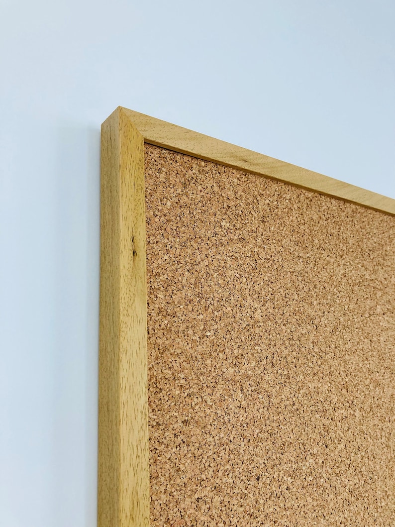 May include: A close-up of the top right corner of a cork board with a natural wood frame. The cork board is a light brown color and the frame is a slightly darker brown.