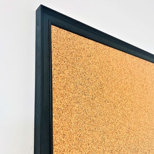 May include: A corkboard with a black frame. The corkboard is made of natural cork and has a textured surface.