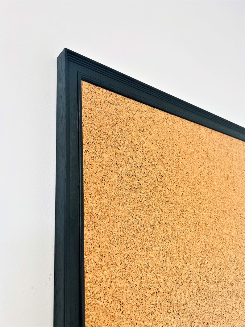 May include: A corkboard with a black frame. The corkboard is made of natural cork and has a textured surface.