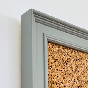 May include: A gray framed corkboard with a textured surface. The frame has a decorative molding around the edge.