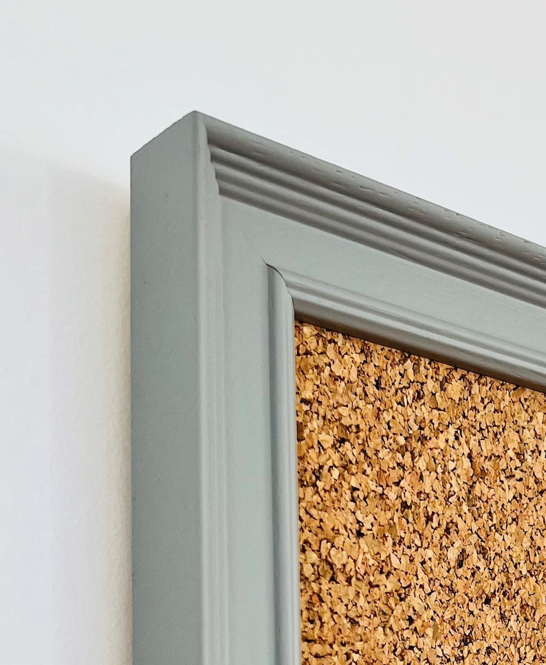 May include: A gray framed corkboard with a textured surface. The frame has a decorative molding around the edge.