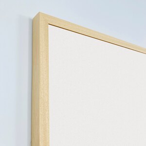 May include: Close-up of the top corner of a light wood frame with a white canvas insert.