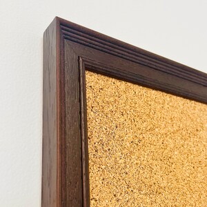 May include: A brown wooden frame surrounds a corkboard. The frame has a slightly raised edge and a textured surface.