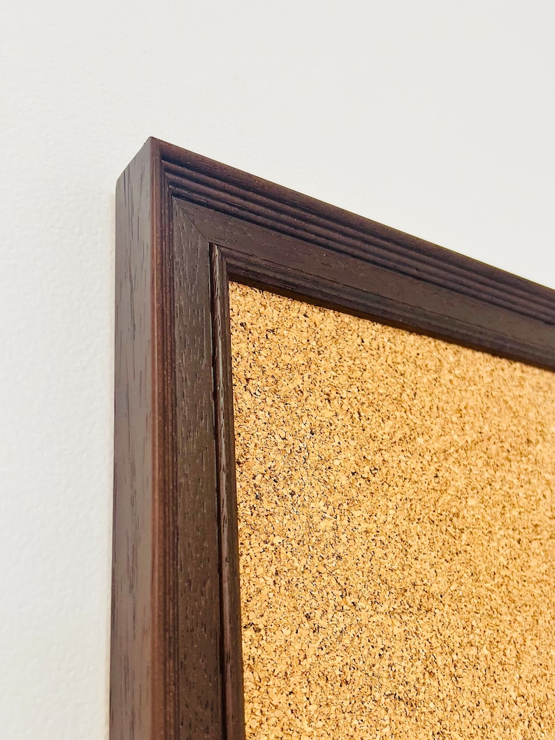 May include: A brown wooden frame surrounds a corkboard. The frame has a slightly raised edge and a textured surface.