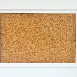May include: A white framed corkboard with a brown cork surface. The corkboard is blank and ready for use.