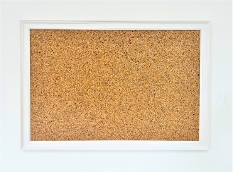 May include: A white framed corkboard with a brown cork surface. The corkboard is blank and ready for use.