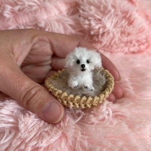 May include: A small white crocheted dog sitting in a brown crocheted basket. The dog has black eyes and a black nose.