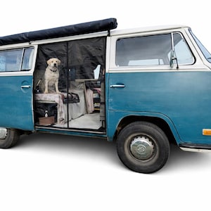May include: A classic blue and white camper van with a black awning. A yellow Labrador sits inside the open door, looking out. The van has a vintage design with round headlights and a split windscreen. The interior is partially visible.