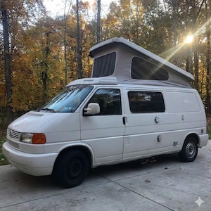 Può includere: Un camper bianco dotato di tetto a soffietto con lati in tessuto grigio e finestre in rete scura. Il veicolo presenta una griglia anteriore, indicatori di direzione arancioni, ruote nere e due porte di accesso circolari sulla fiancata.