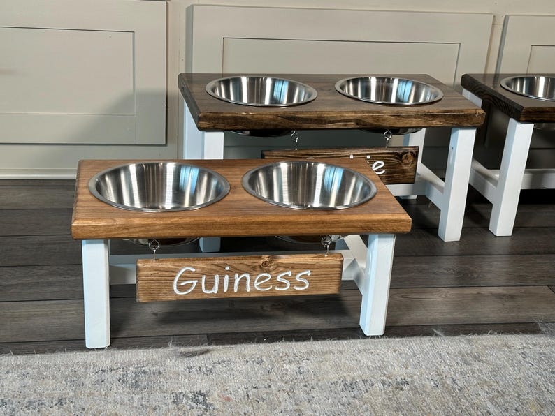 May include: A wooden dog bowl stand with two stainless steel bowls. The stand is painted white and has a sign that says "Guinness".