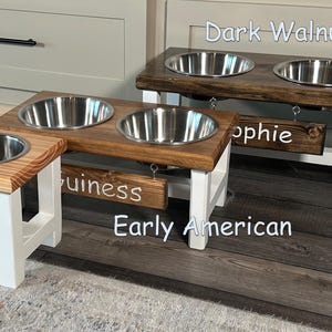 May include: Four elevated dog bowls in different wood finishes: Pecan, Early American, Dark Walnut, and Maple. Each bowl has a personalized name tag: Tiko, Guinness, Sophie, and Belle.