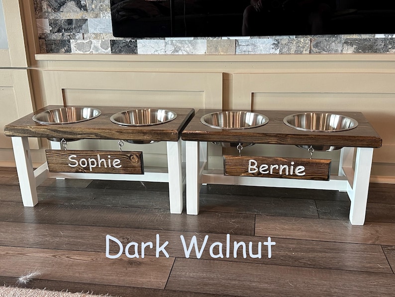 May include: Double elevated dog bowl stand in dark walnut with white legs and stainless steel bowls. The stand has two personalized signs that read "Sophie" and "Bernie".