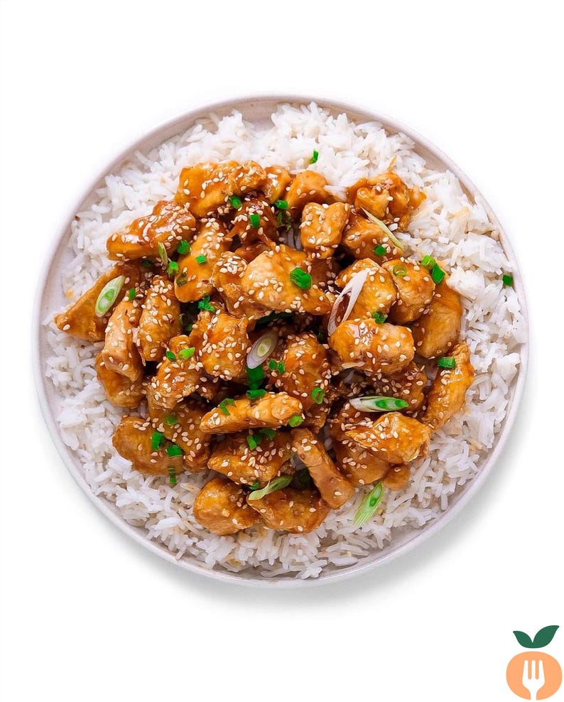 May include: A plate of white rice topped with sesame chicken, garnished with green onions and sesame seeds.