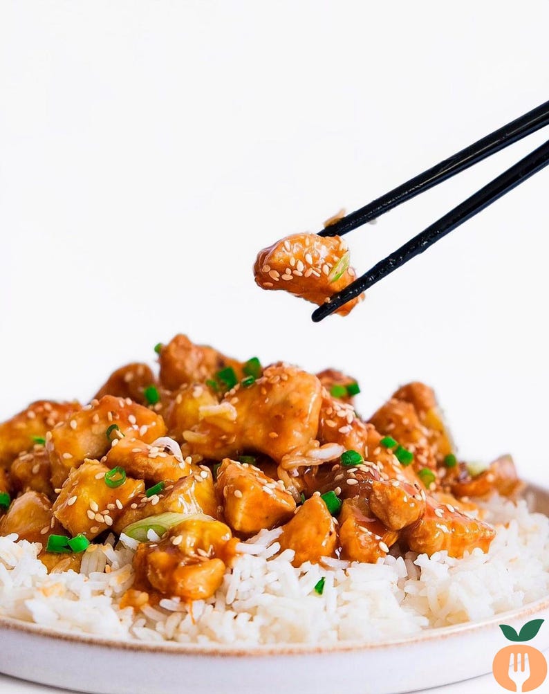 May include: A plate of chicken and rice with a sesame seed and soy sauce glaze. The chicken is being lifted with chopsticks.