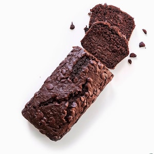 May include: A chocolate chip loaf cake, partly sliced, on a white background. The cake is dark brown with chocolate chips. Two slices are separated from the loaf, with a few chips scattered around.
