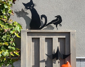 May include: Black metal Halloween decorations including a cat, a crow, and bats hanging on a wooden fence. An orange pumpkin sits on a wooden base. The cat and crow are perched on top of the fence.