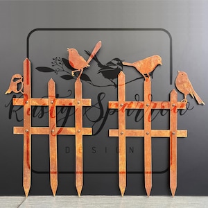 May include: A metal fence decoration featuring birds. The fence is made of a rusty brown metal with a cross-hatch pattern. Several metal birds are perched on the fence. The text "Rusty Sparrow Design" is visible on the dark background.