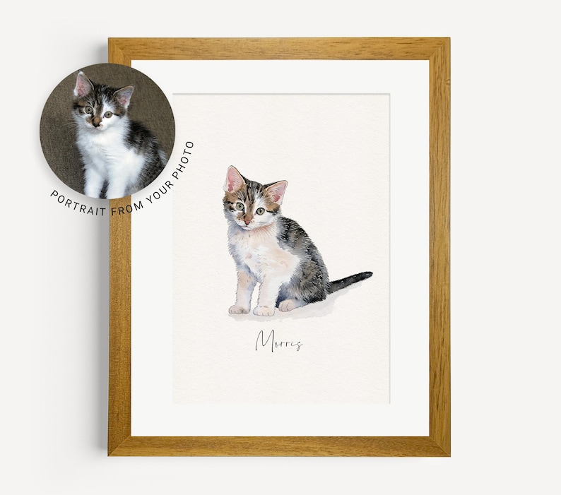 May include: A watercolor painting of a tabby cat named Morris. The cat is sitting with its front paws together and its tail curled behind it. The painting is framed in a light brown wood frame.
