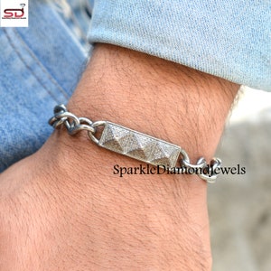 May include: A silver bracelet with a rectangular centerpiece featuring a pyramid design, studded with small, sparkling stones. The bracelet has a chain-link style and is worn on a wrist. The text "Sparkle Diamond Jewels" is visible.