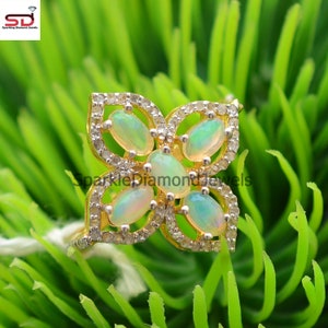 Könnte beinhalten: Ein goldener Ring mit einem Blumendesign mit fünf ovalen Opalen und kleinen Diamanten. Der Ring ist vor einem grünen Hintergrund platziert.