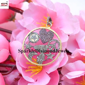 May include: A silver and gold pendant with a circle design featuring a heart, star, peace sign, cloud, and hand. The pendant is set with small diamonds and pink stones.
