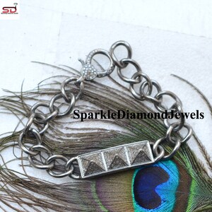 May include: A silver-toned bracelet with a rectangular centerpiece featuring three pyramid-shaped designs. The bracelet has a chunky chain link design and a clasp with small, sparkling embellishments. The text "SparkleDiamondJewels" is visible.