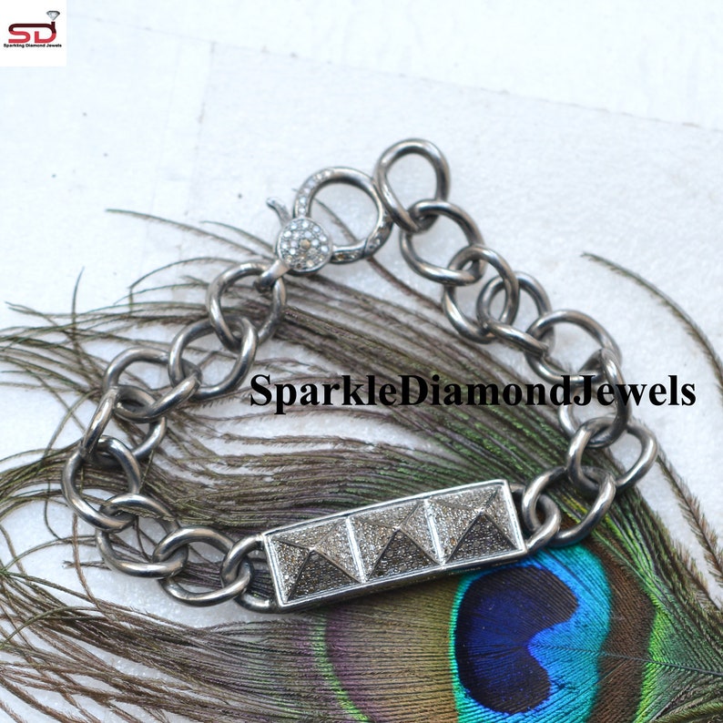 May include: A silver-toned bracelet with a rectangular centerpiece featuring three pyramid-shaped designs. The bracelet has a chunky chain link design and a clasp with small, sparkling embellishments. The text "SparkleDiamondJewels" is visible.