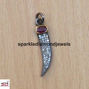 May include: A silver pendant shaped like a tooth, encrusted with small white diamonds and topped with a red gemstone.