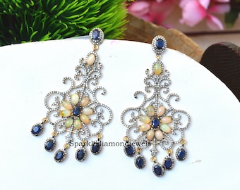 May include: A pair of silver dangle earrings with a floral design. The earrings are adorned with white opals and blue sapphires. The earrings are approximately 2 inches long.