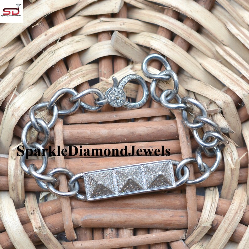 May include: A silver bracelet with a rectangular center piece featuring three pyramid-shaped designs. The bracelet has a chain link design and a clasp closure. The text "SparkleDiamondJewels" is visible on the image.