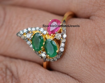 May include: A gold ring with two green oval emeralds and a pink gemstone surrounded by small diamonds. The ring is set in a leaf-shaped design. SparkleDiamondJewels