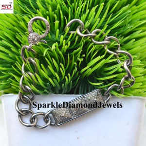 May include: A silver bracelet with a large chain link design. The bracelet features a rectangular bar with a pyramid design and a clasp, both encrusted with small, sparkling stones. The text "SparkleDiamondJewels" is visible on the bar.