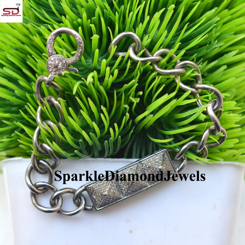 May include: A silver bracelet with a large chain link design. The bracelet features a rectangular bar with a pyramid design and a clasp, both encrusted with small, sparkling stones. The text "SparkleDiamondJewels" is visible on the bar.
