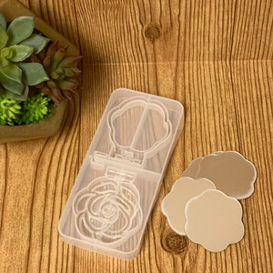 May include: A clear plastic mold for making resin crafts. The mold has two sections, one with a rose design and the other with a flower design. Three small, round, flower-shaped mirrors are also included.
