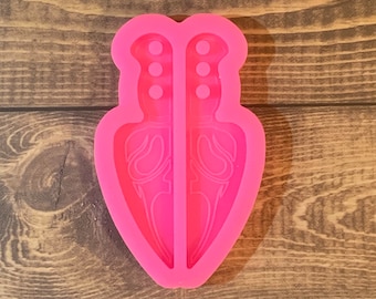 May include: Pink silicone mold for making two double-edged knives with decorative details.