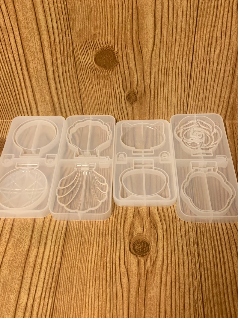 May include: Four clear silicone molds for resin casting. Each mold has two cavities. The top row features a circle, a seashell, a cat face, and a rose. The bottom row features a starburst, a seashell, a cat face, and a rose.