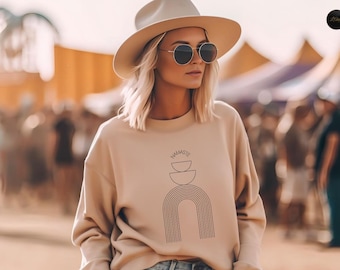 Puede incluir: Una sudadera beige con un diseño gráfico de un arcoíris y la palabra "namaste" en texto negro.
