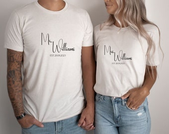 Peut inclure: Deux t-shirts blancs avec du texte noir. Le t-shirt de gauche dit "Mr. Williams EST 23.08.2023". Le t-shirt de droite dit "Mrs. Williams EST 23.08.2023".