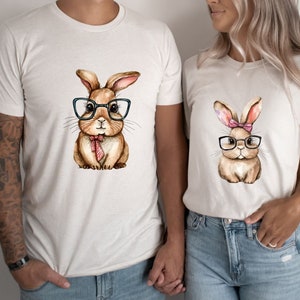 May include: Two white t-shirts with a brown bunny wearing glasses and a bow tie on one shirt and a brown bunny wearing glasses and a pink bow on the other shirt.