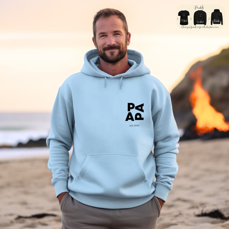 Op de afbeelding: Een lichtblauwe hoodie met een zwart logo met de tekst "PAPA est. 1990" op de voorkant.