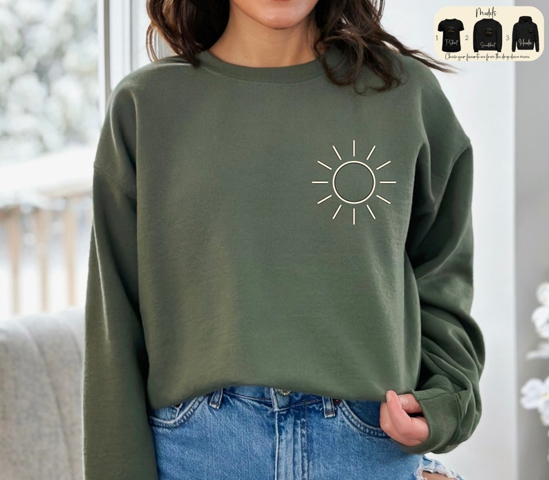 May include: A green sweatshirt with a white sun graphic on the front. The sweatshirt is a relaxed fit and has long sleeves.