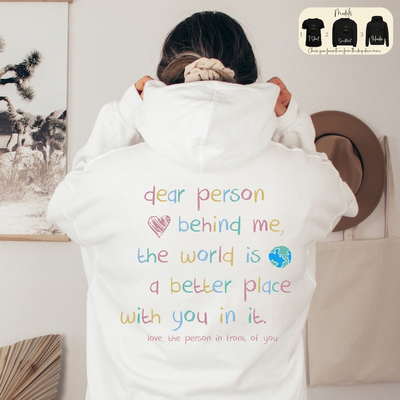 May include: White hoodie with a colorful message on the back that reads "dear person behind me, the world is a better place with you in it. love, the person in front of you".