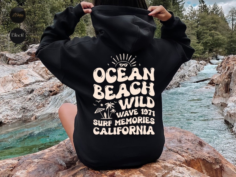 May include: Black hooded sweatshirt with a white graphic print that says "Ocean Beach Wild Wave 1971 Surf Memories California".
