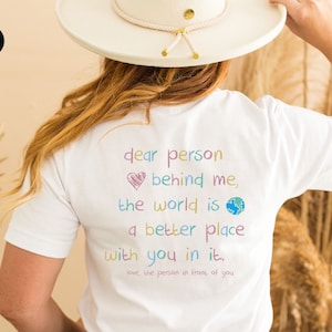 May include: White t-shirt with a colorful message that reads "dear person behind me, the world is a better place with you in it. love, the person in front of you".
