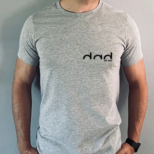 May include: A gray t-shirt with a black graphic that says "dad est. 2023".