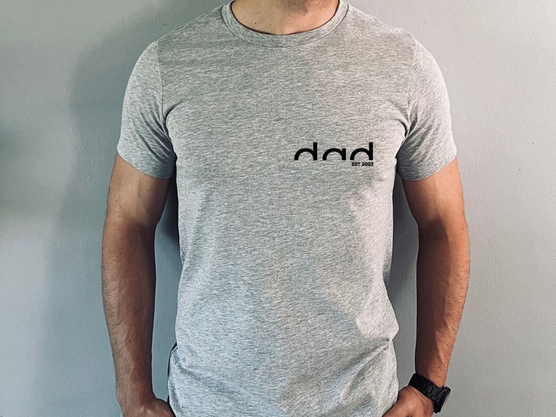 May include: A gray t-shirt with a black graphic that says "dad est. 2023".