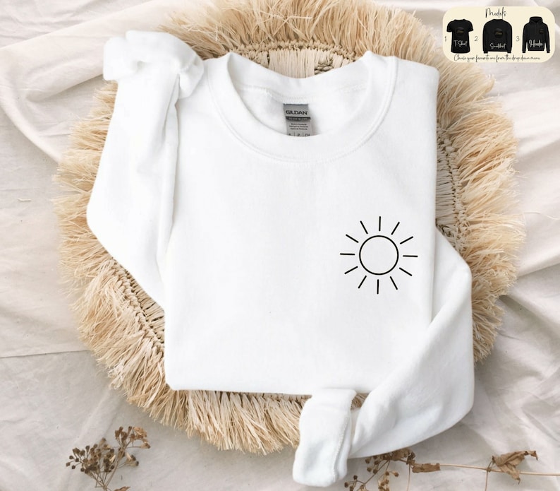 May include: White sweatshirt with a simple black sun graphic on the front. The sweatshirt is made of a soft, comfortable material.