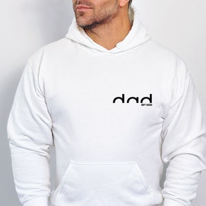 May include: White hooded sweatshirt with the word "dad" in black text and the words "est 2023" in smaller black text below.