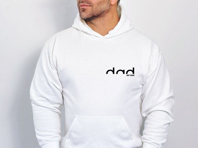 May include: White hooded sweatshirt with the word "dad" in black text and the words "est 2023" in smaller black text below.