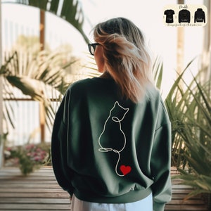 a woman wearing a green sweatshirt with a cat drawn on it